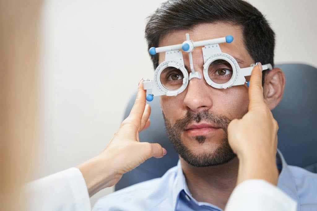 Oculist putting trial frame on man eyes