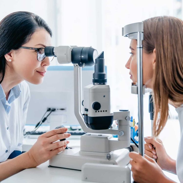 Adult female doctor ophthalmologist checking eye vision of young girl in modern clinic